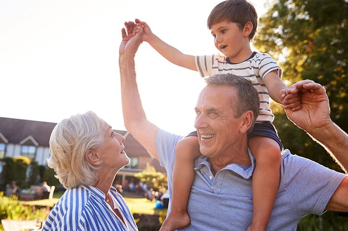 Family enjoying outdoor time with a young boy on grandfather's shoulders.