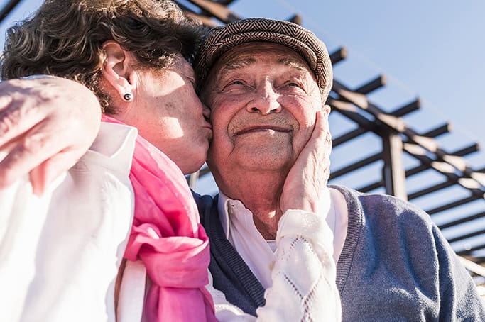 Elderly man receiving a loving kiss from a young girl outdoors.